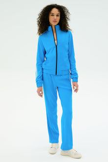 A person stands facing forward in the SPLITS59 Fox Techflex Jacket in Riviera/White and white sneakers, set against a plain white background.