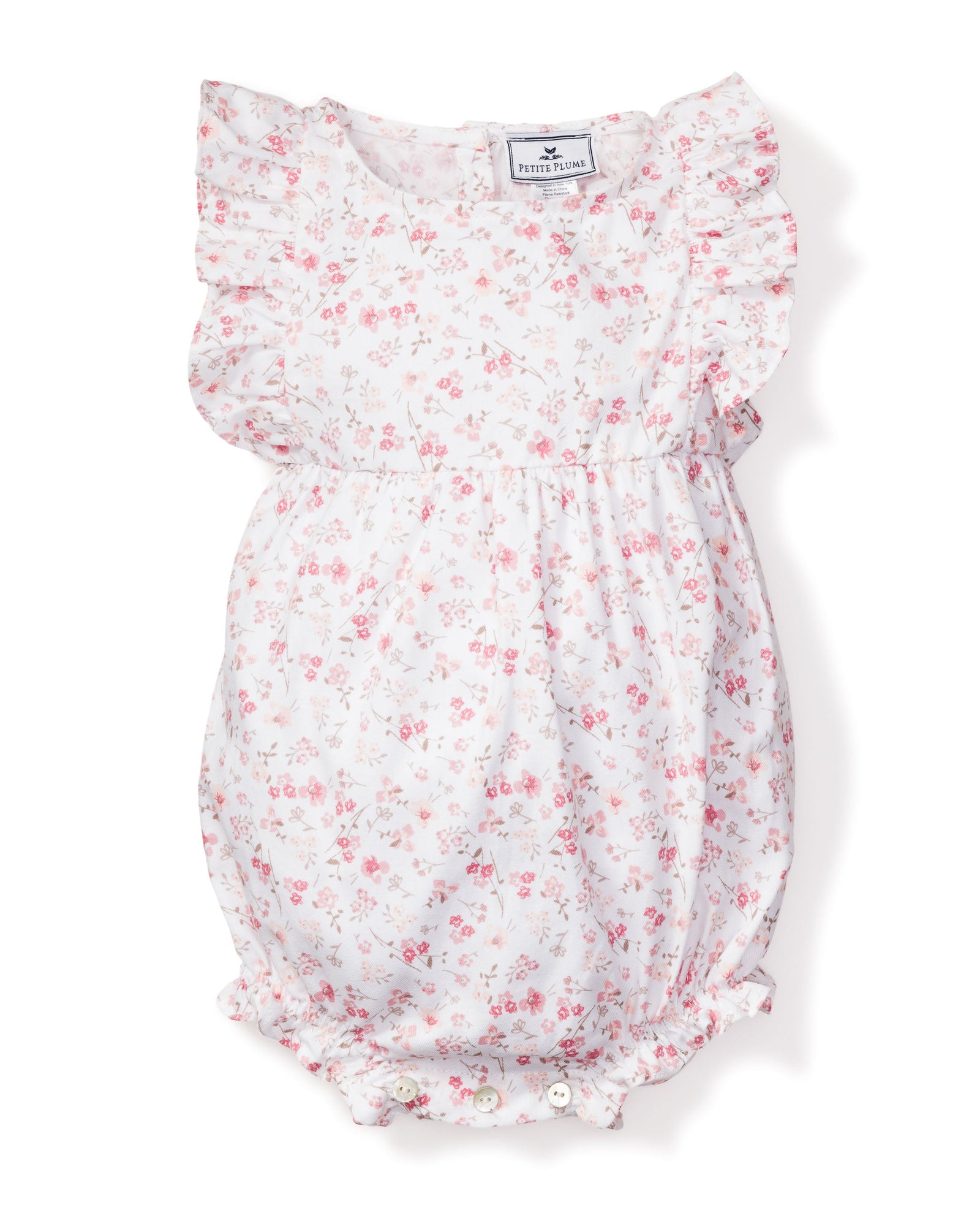 The Babys Twill Ruffled Romper in Dorset Floral by Petite Plume is a charming Victorian-inspired piece featuring pink flowers on white with ruffled sleeves, a gathered waist, and visible bottom buttons for classic elegance and modern comfort.