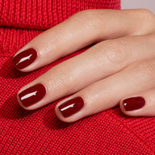 A hand with neatly manicured nails painted in Manucurist’s Dark Pansy, a glossy burgundy shade, rests on red knit fabric, perfectly matching the velvet red sweater underneath.