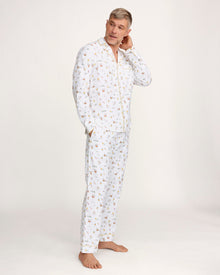 A man with short gray hair wears the Men's Twill Pajama Set in Easter Frolic—white pants and a long-sleeve top with a small, colorful print—standing barefoot against a plain light background.