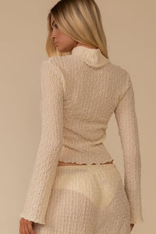 Cream textured long-sleeve top with cowl neckline and fitted waist, shown on model from back view.