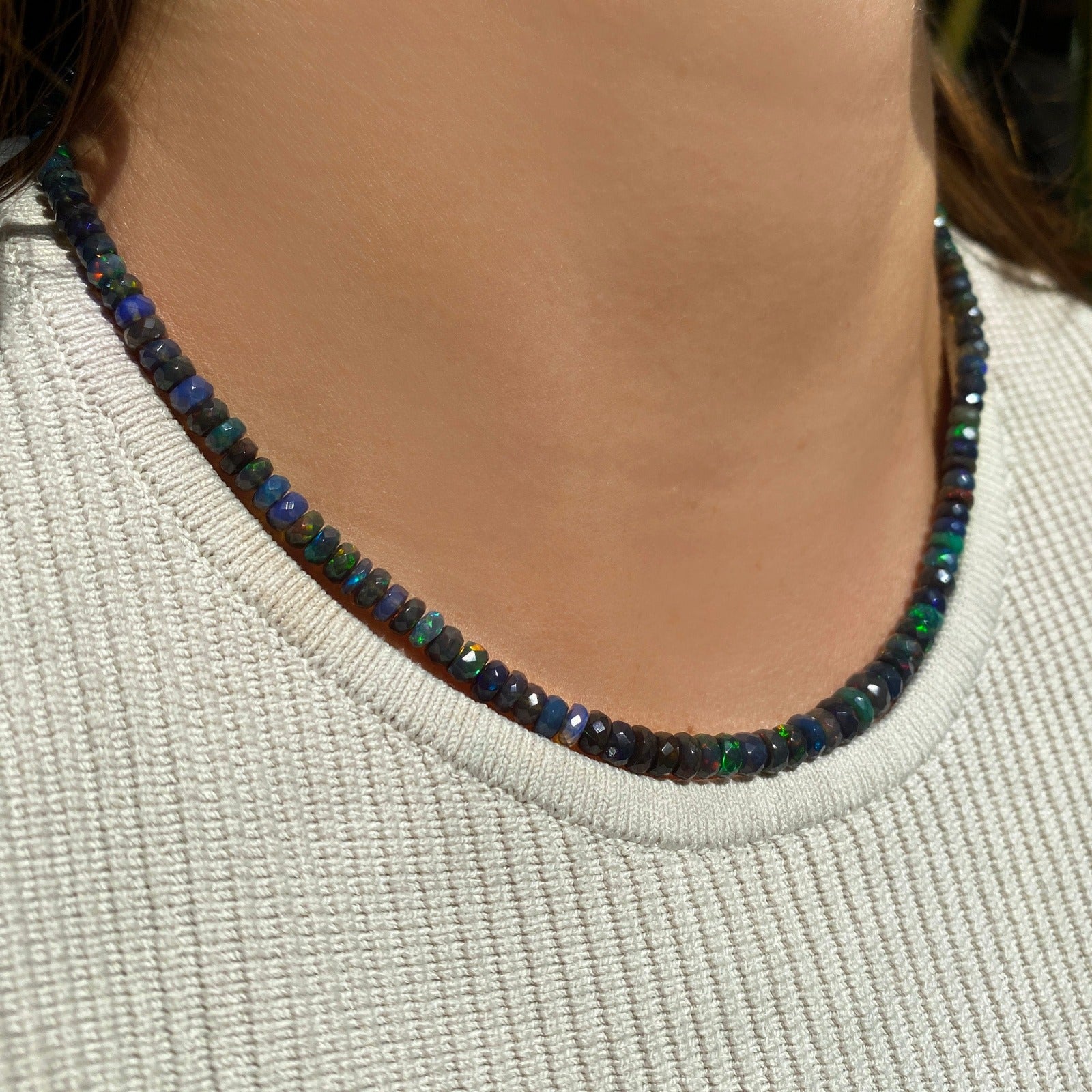 Shimmering beaded necklace made of faceted opals in shades of black, green, and blue on a gold linking ovals clasp. 
