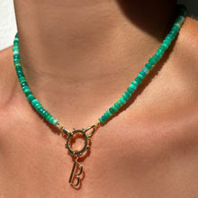 Shimmering beaded necklace made of faceted opals in shades of green on a gold linking ovals clasp. Styled on a neck layered with a round charm lock and B letter charm.