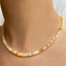 Shimmering beaded necklace made of smooth opals in shades of yellow, tan and white on a gold linking ovals clasp on a neck