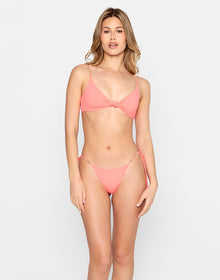 Model wearing the Brielle Knot Top and Brielle Tie Side Skimpy Bottom in coral pink with shell strap and ring details, from the latest swimwear collection.