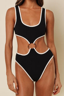Black one-piece swimsuit with cream binding on neckline, armholes, and leg openings, featuring cutout back with ring detail.