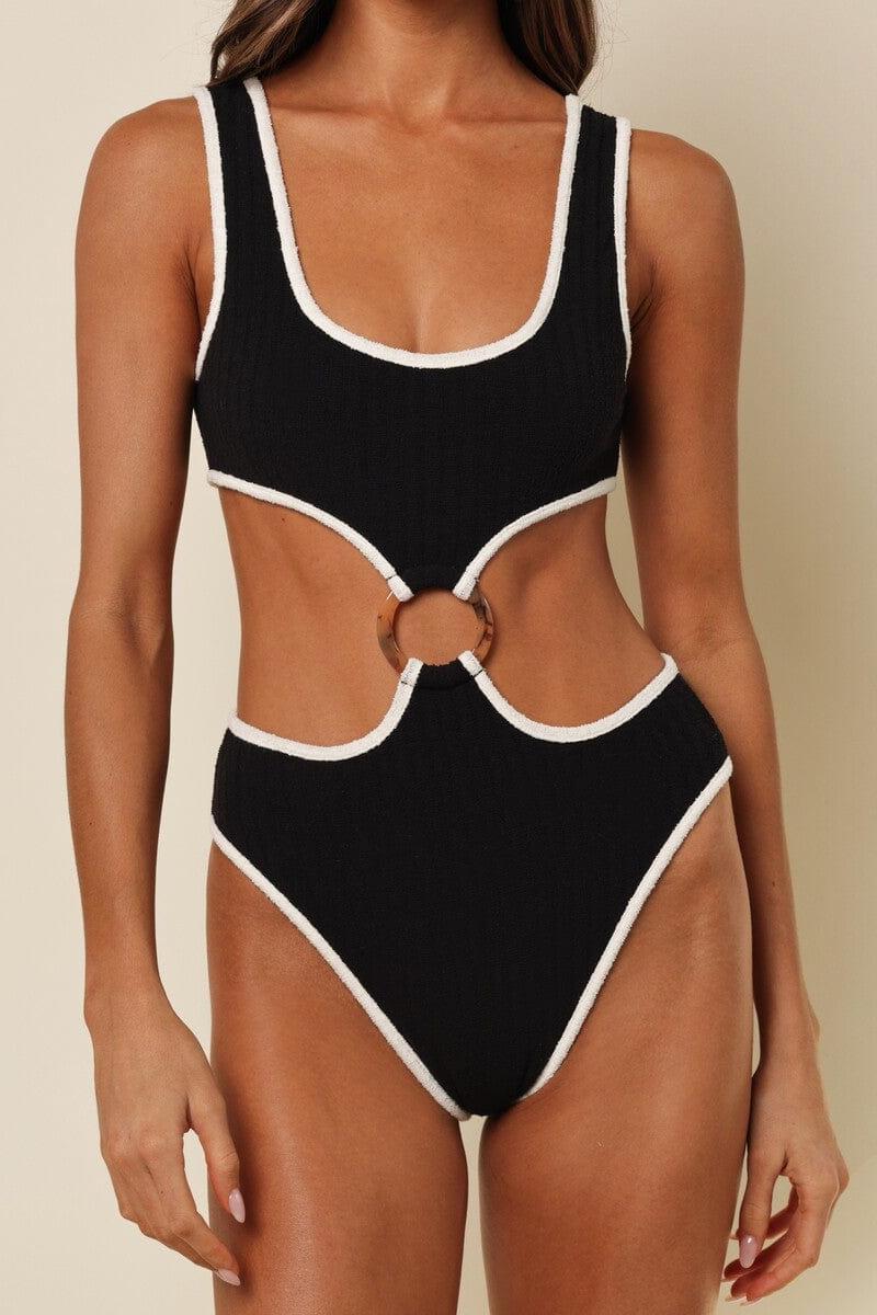 Black one-piece swimsuit with cream binding on neckline, armholes, and leg openings, featuring cutout back with ring detail.