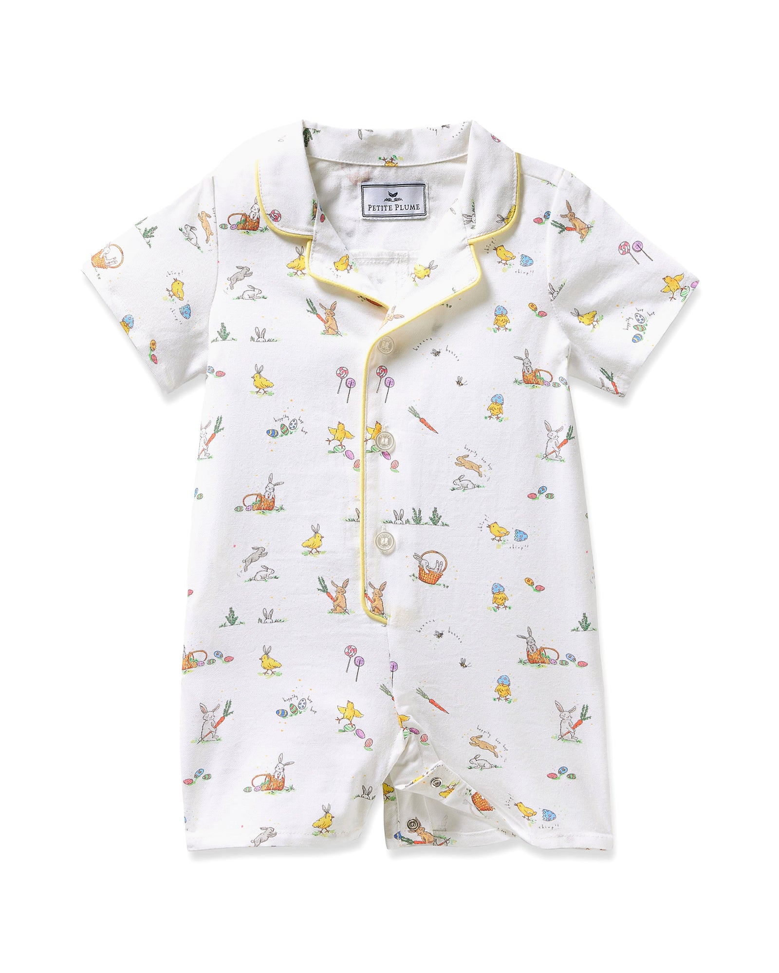 A young child with blonde hair wears the Baby's Twill Summer Romper in Easter Frolic—white with colorful animal prints and yellow trim—standing against a plain light background, holding two wooden blocks and looking to the side.