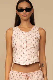 Pale pink sleeveless tank top with small red cherry print throughout and button front closure.