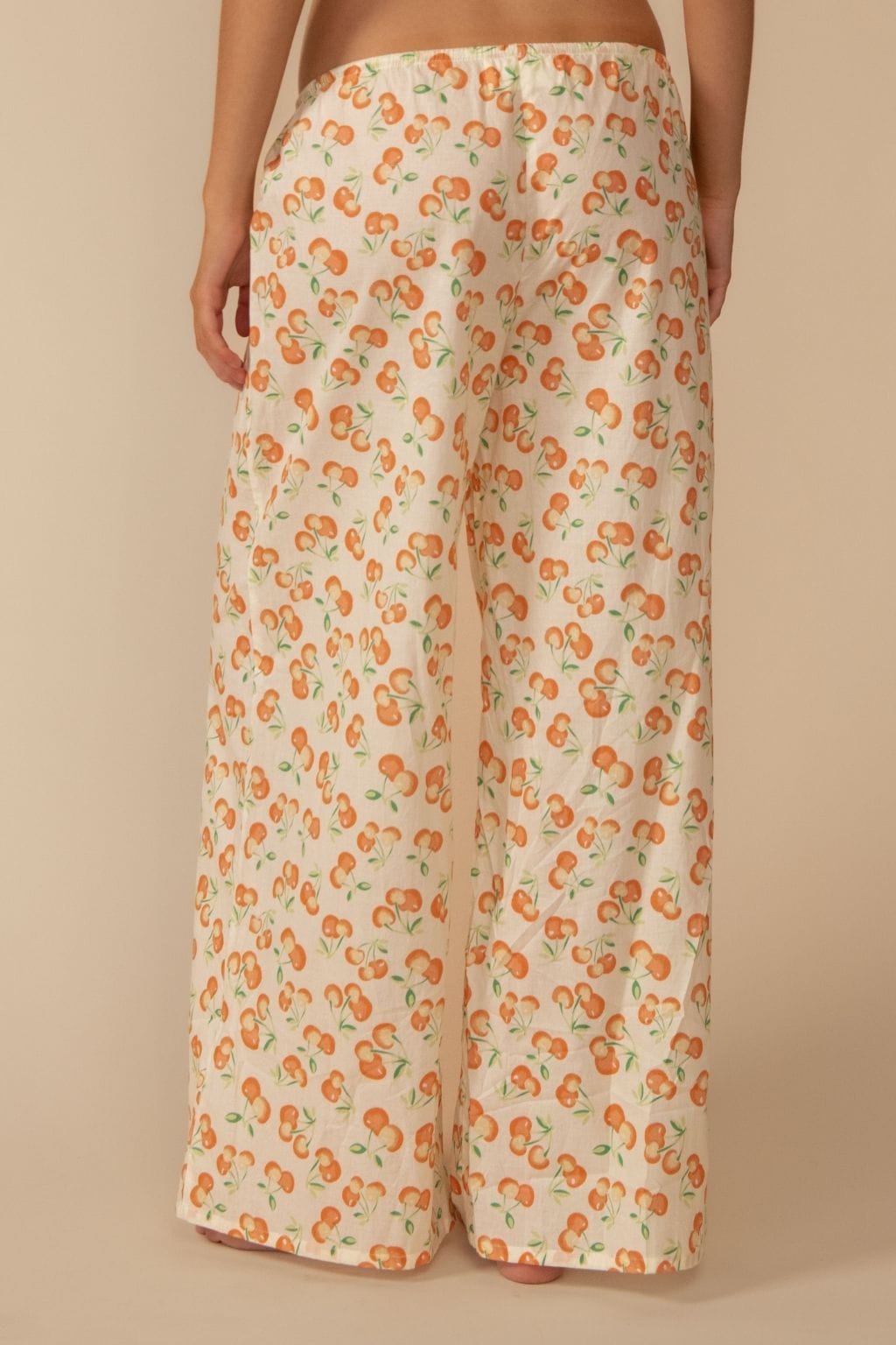 Cream-colored wide-leg pants with orange cherry print and drawstring waist, shown from behind on model.