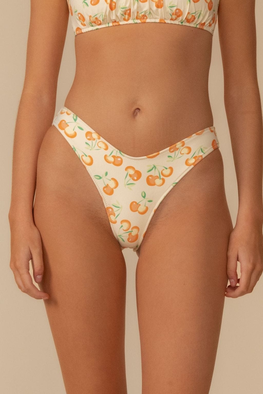 Cream bikini bottom with orange cherry and green leaf print and zig-zag stitching at waistband and leg openings.