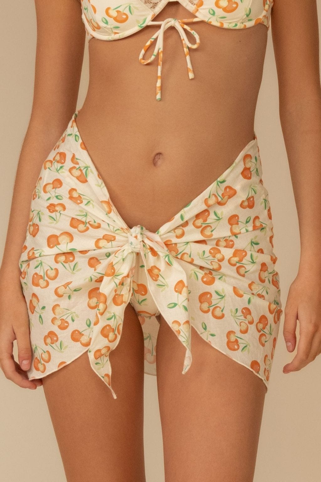 Cream-colored sarong with orange fruit and green leaf print, tied at sides with string closures.