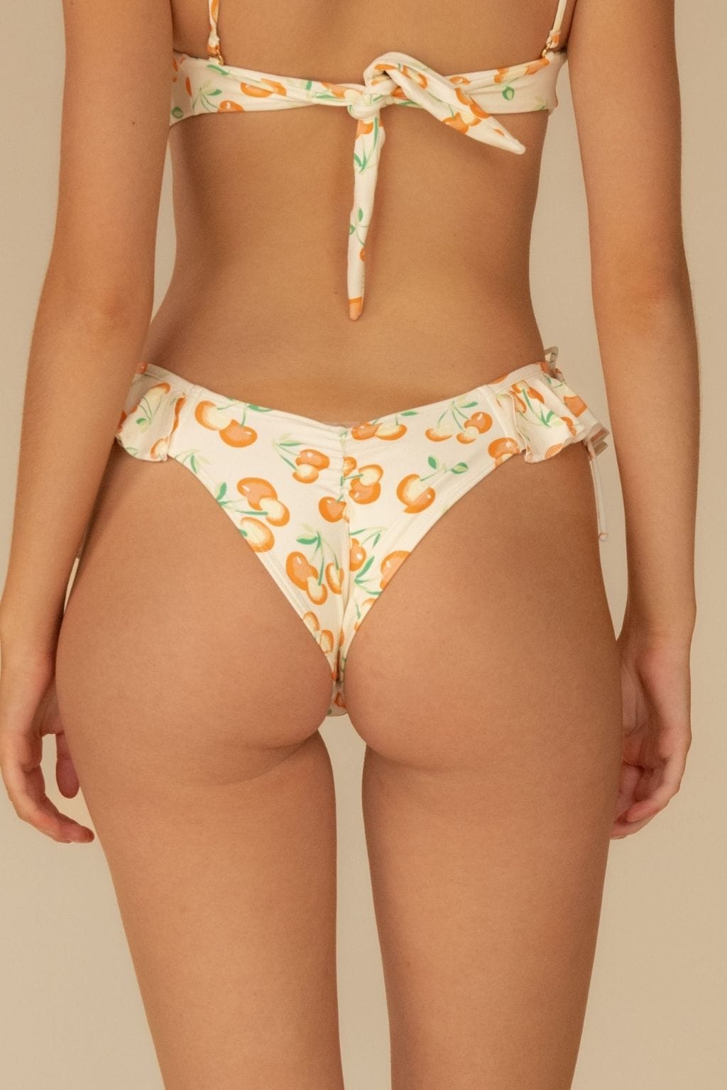 Cream bikini bottom with orange cherry print and ruffled edges at leg openings and waistband.