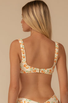 Cream bikini top with orange cherry and green leaf print, wide shoulder straps, and hook-and-eye back closure.