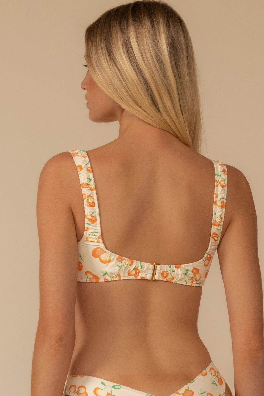 Cream bikini top with orange cherry and green leaf print, wide shoulder straps, and hook-and-eye back closure.