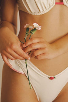 Cream bikini bottom with raspberry binding at waistband and small floral embroidery detail at hip.