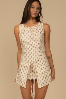 Sleeveless cream dress with small dark floral print and front drawstring tie detail.