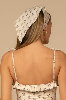 Cream-colored scarf with small blue floral print, tied around head with string closures on sides.
