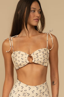 Cream bandeau bikini top with small dark floral print and tie shoulder straps featuring center cutout detail.