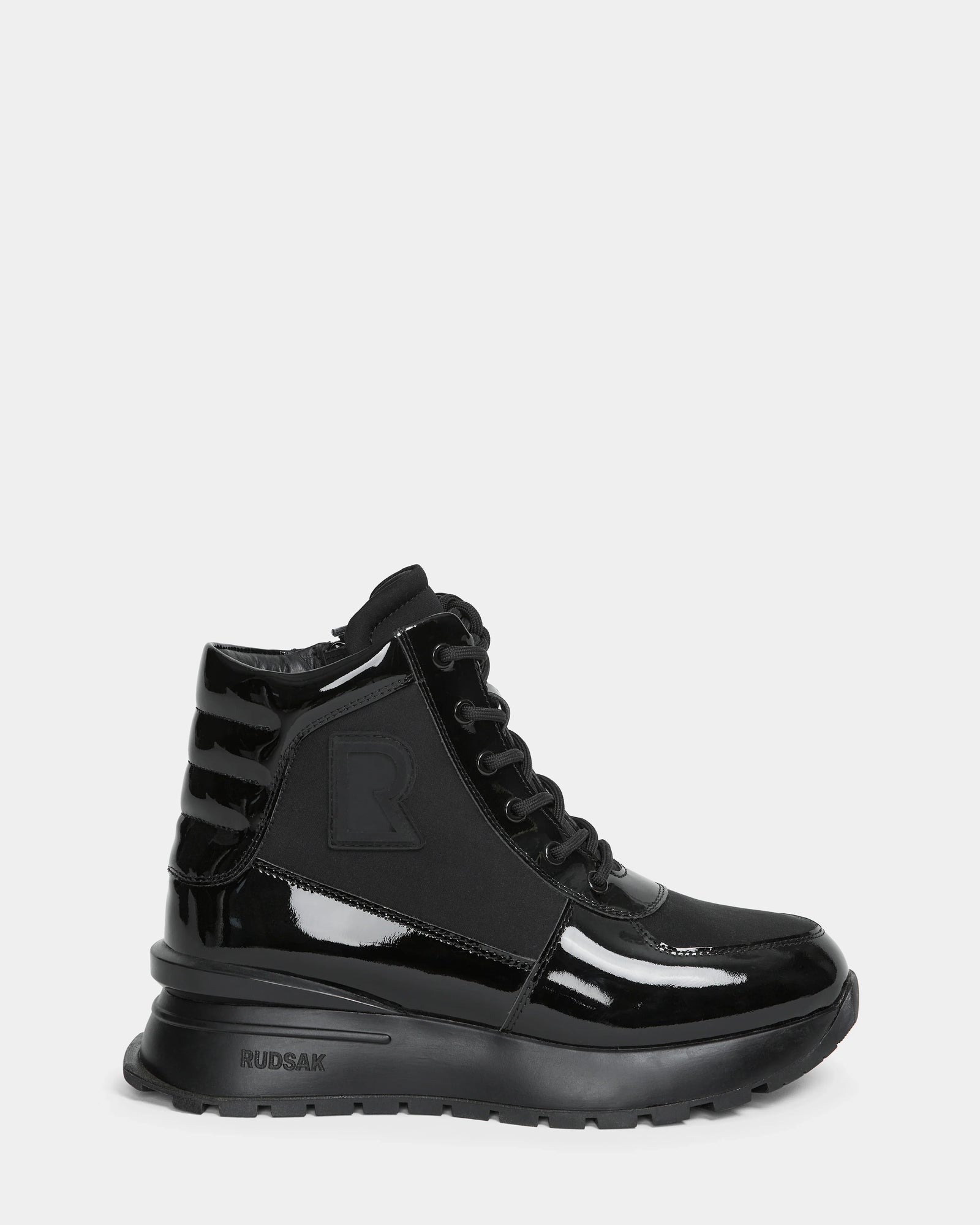 The CHELSA - L224505 Black by Rudsak is a women’s sneaker boot in black patent leather with a chunky sole, lace-up front, waterproof zipper, ribbed heel, and subtle side R logo. Glossy and weather-resistant for stylish wear.