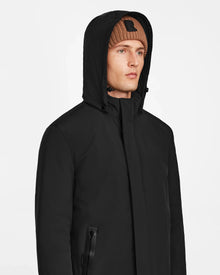 A man in a brown knit beanie and the Rudsak NATAN - M124519 Black men’s parka looks off to the side against a plain white background.