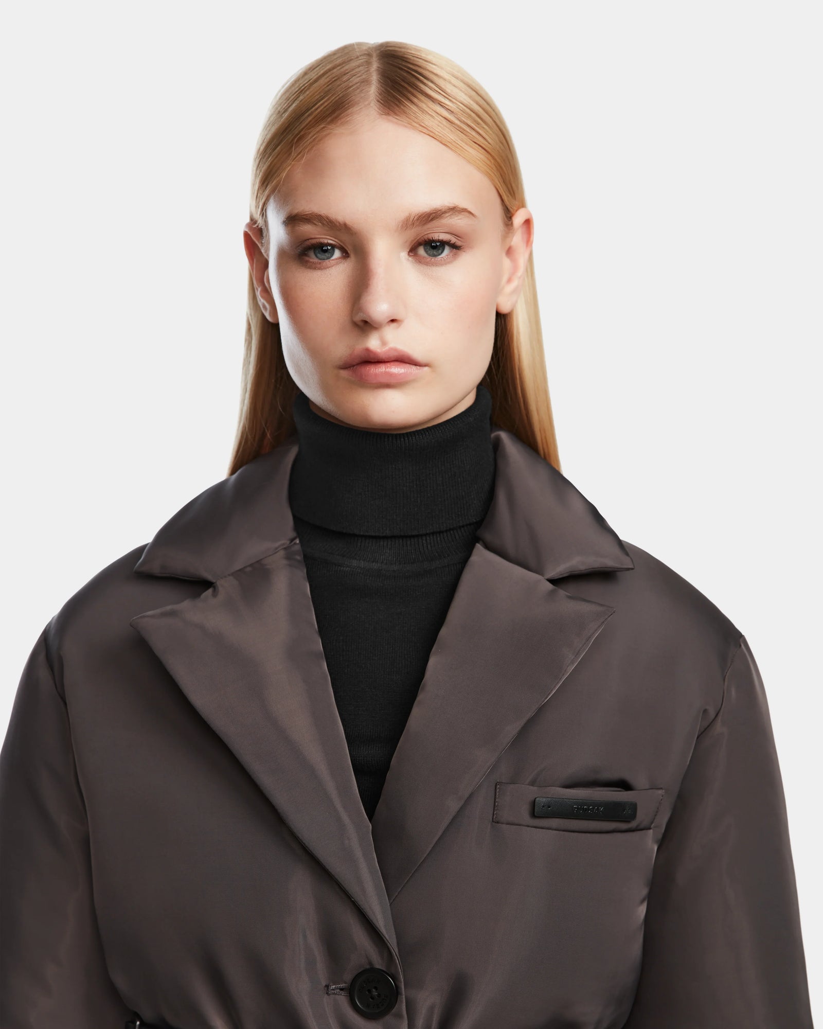 A woman with straight blonde hair models the Rudsak PAOLA - 8124547 Grey womens down blazer over a black turtleneck, looking directly at the camera with a neutral expression against a plain light background.