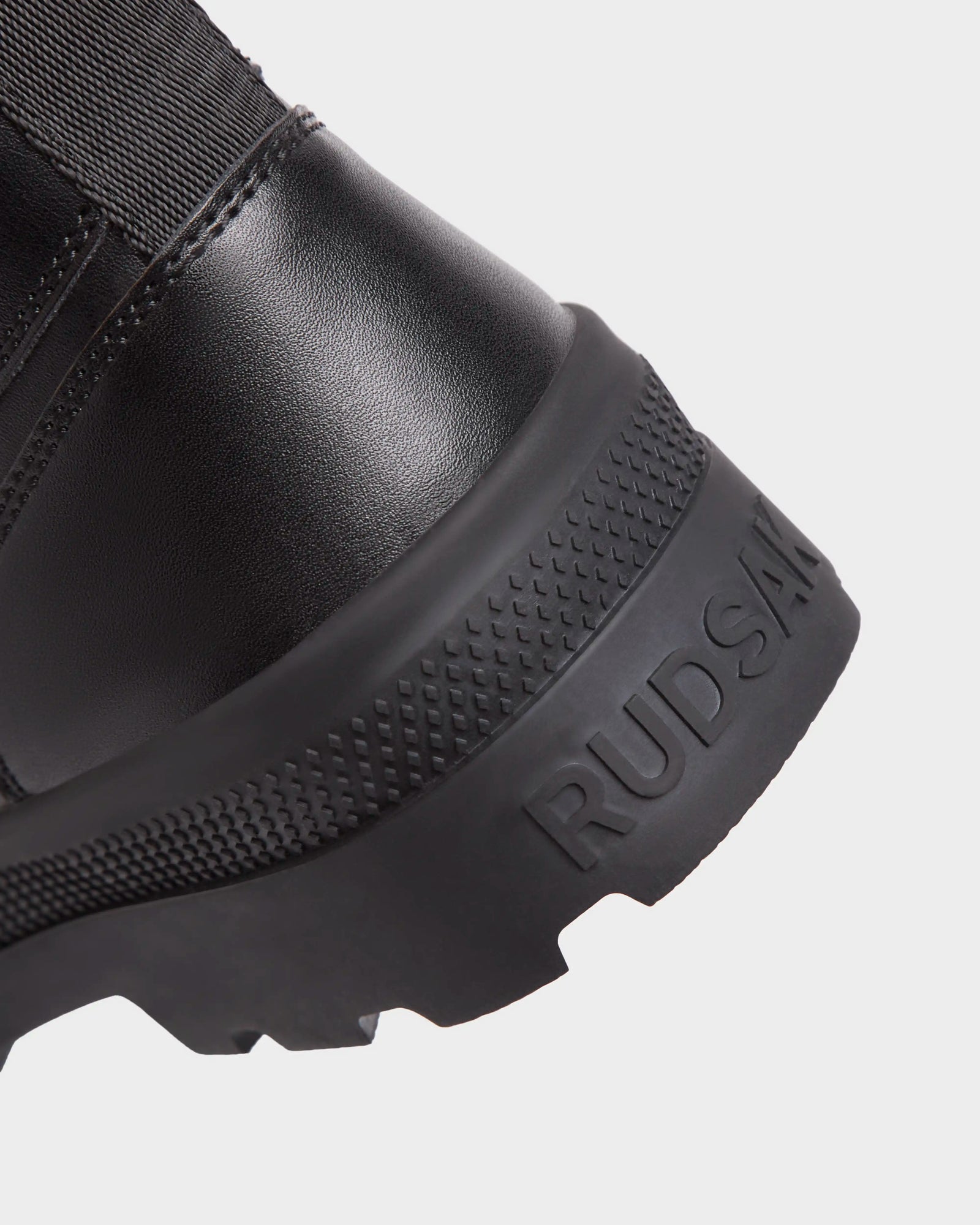Close-up of the heel of RITA - L222502 Black women's winter boot. Features a textured rubber sole and weather-treated leather with "Rudsak" embossed on the side.