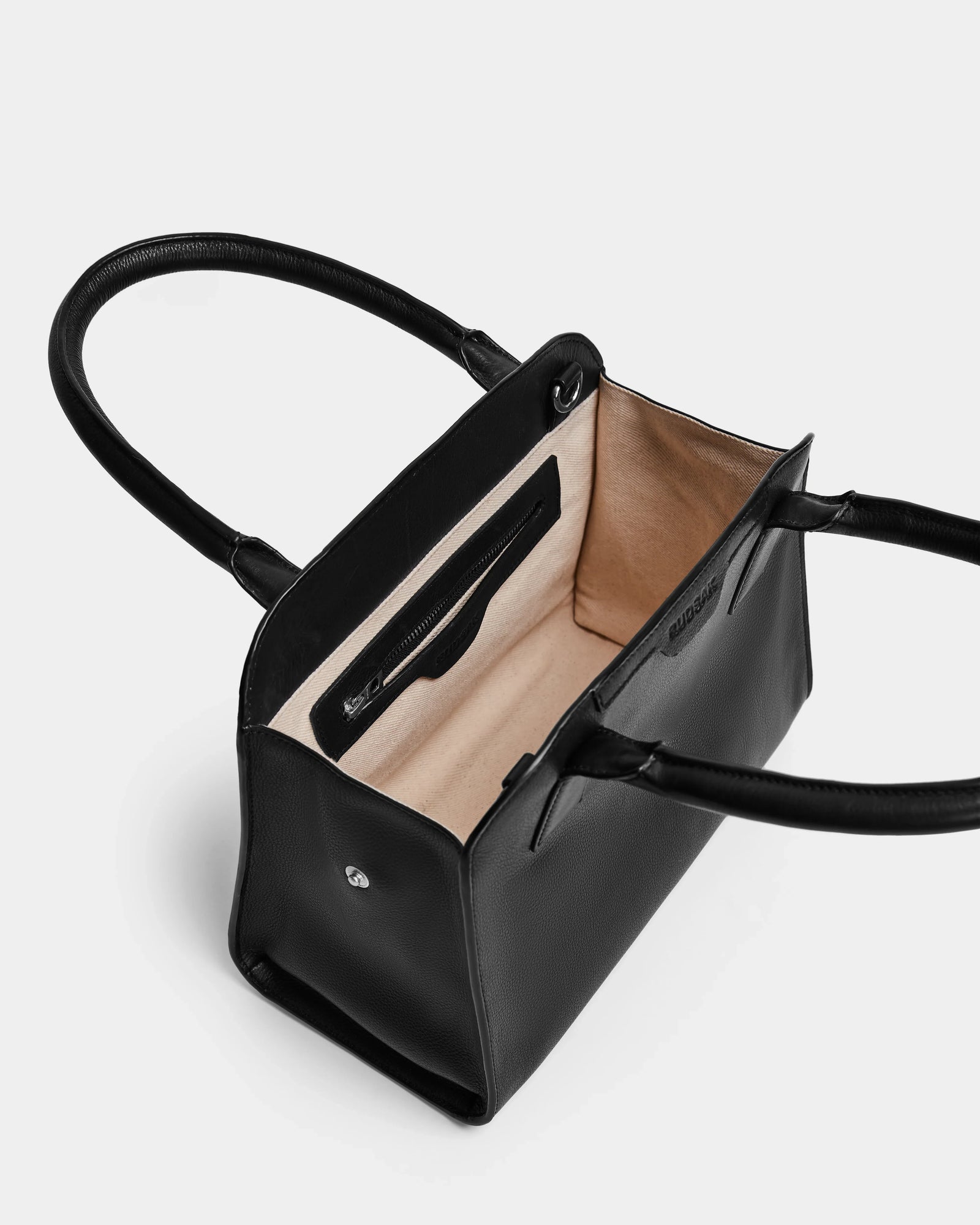 The Rudsak YASMINA - 8324527 Black leather tote features two handles, a beige interior lining, an inner zipper pocket, and a small branded patch inside.