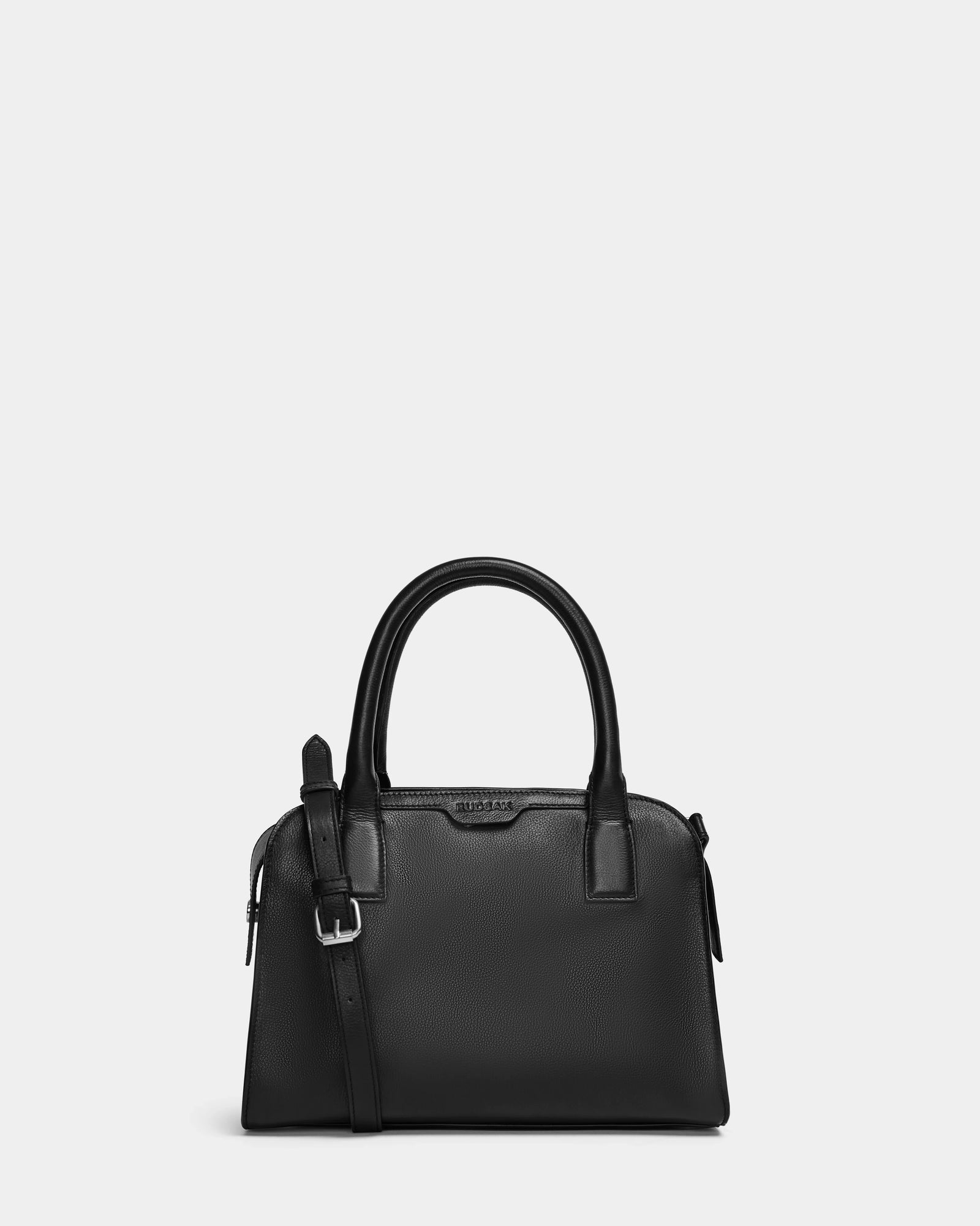 Structured and sleek, the Rudsak YASMINA - 8324527 black leather tote features two rounded handles, a detachable shoulder strap with silver buckle, and a crisp rectangular shape, set against a plain light gray background.