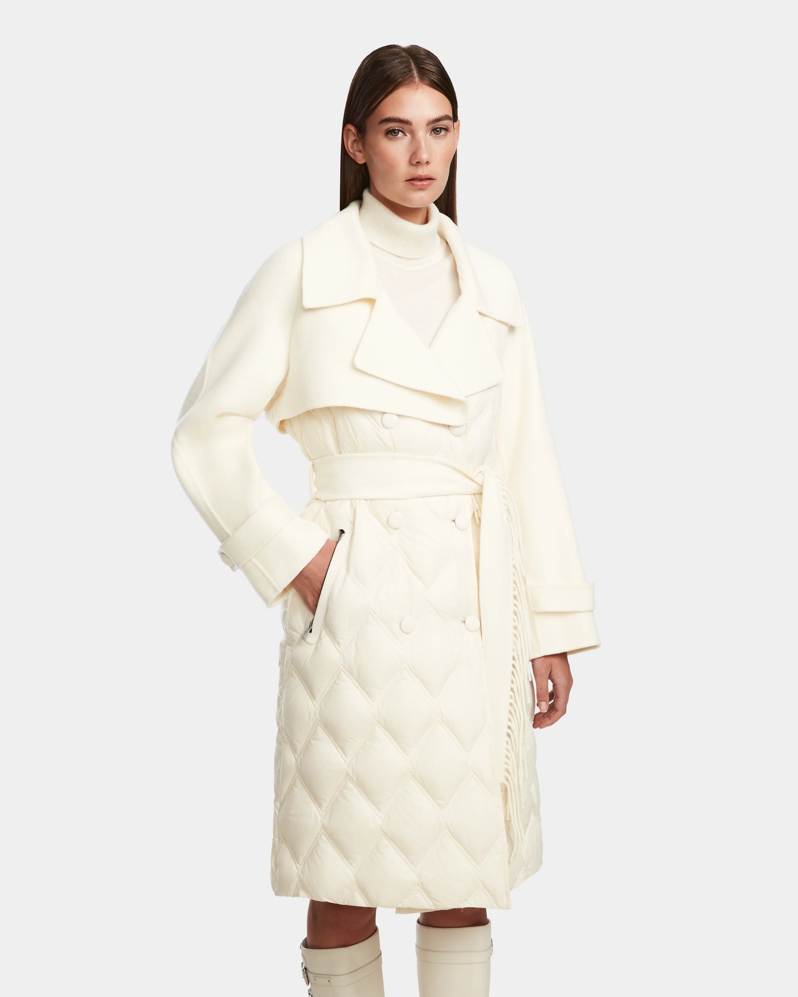 A woman stands with one hand in her pocket, modeling the Rudsak ZOE - 8124711 Iceland off-white quilted down trench with a wide collar, belted waist, and double-breasted buttons against a plain background.