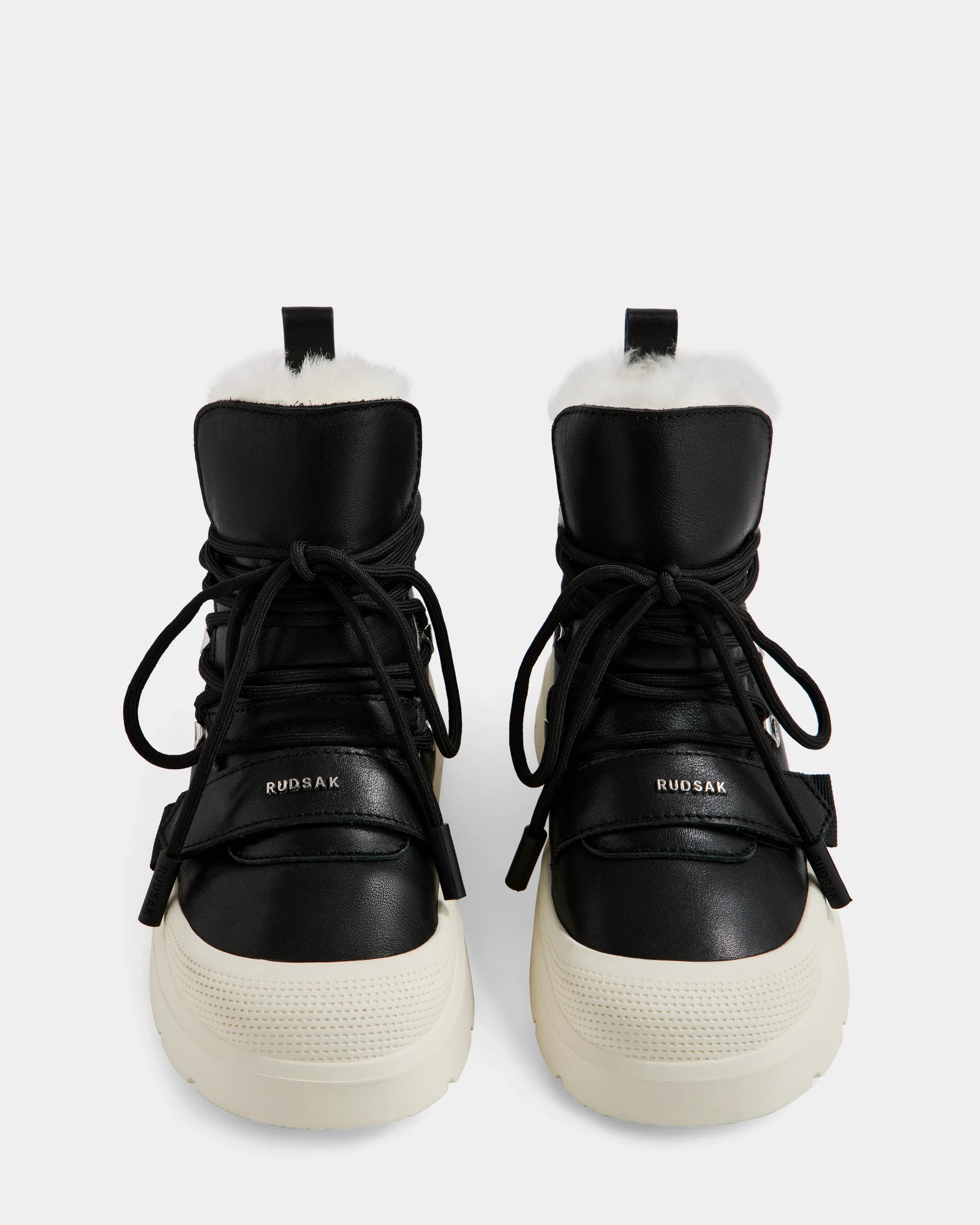 A pair of Rudsak ALEXEY L - L225518 Black women’s leather winter boots with thick white soles, black laces, and visible plush wool lining, shown from the front on a plain white background.