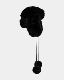The Rudsak DEMI - L425539 Black is a women’s faux-fur aviator hat featuring ear flaps and long strings with fluffy pom-poms, shown against a plain light gray background.
