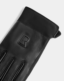 A close-up of Rudsak's EDDIE - 6425037 Black men's leather glove with decorative stitching and an embossed “R” on the back, photographed against a light gray background. These stylish gloves are ideal for staying warm in winter.