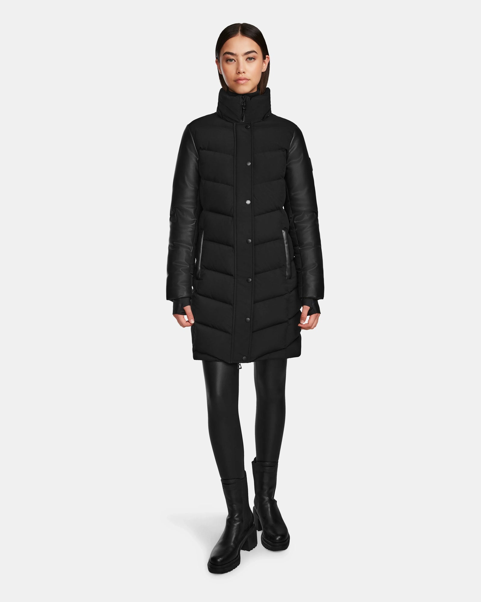 A woman stands facing forward, wearing the Rudsak ELSA - L123535 Black quilted down puffer, black leggings, and black ankle boots against a plain white background.