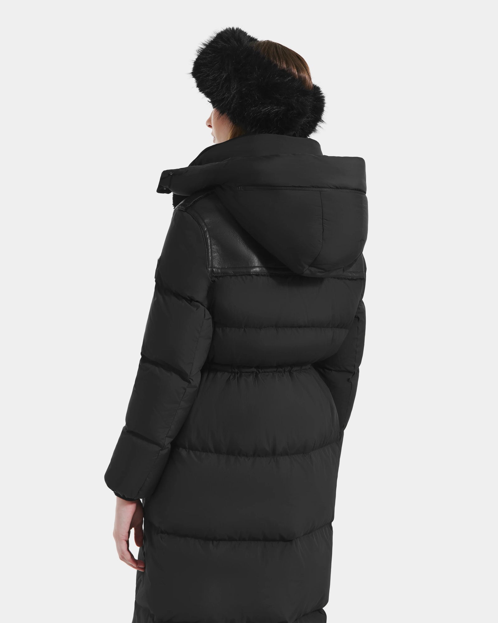 A woman is shown from the back wearing the Rudsak EMBER M-L - L125543 Black long down puffer coat with removable hood and a black furry hat, set against a plain light background.