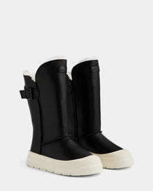 The Rudsak KLAIR L - L225519 Black are women’s mid-calf leather boots with white chunky rubber soles, side zippers, buckles, and white shearling trim, shown standing upright on a plain background.