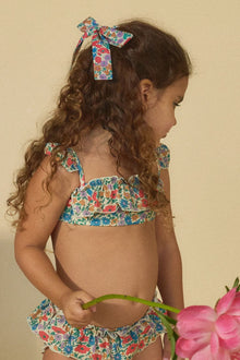 Multicolored floral hair ribbon with bow tied in dark brown curled hair on child.
