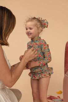 Toddler wearing multicolored floral rashguard with long sleeves and matching hair bow.