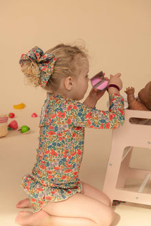Toddler wearing colorful floral long-sleeve rashguard with red, orange, and blue flowers on cream background.