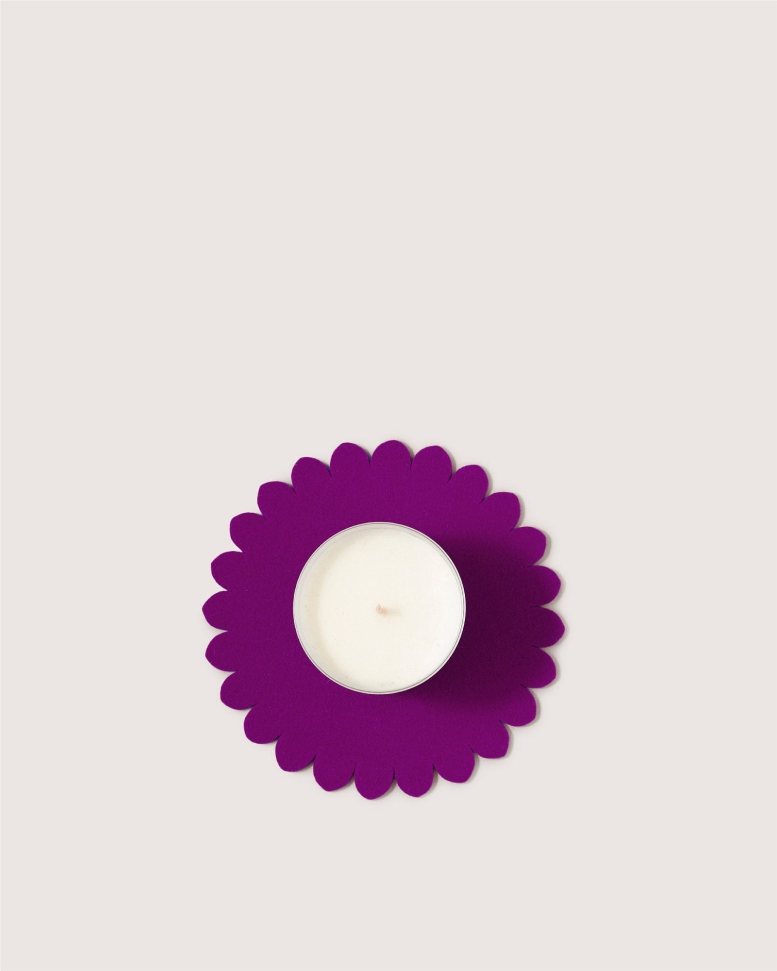 A white tealight candle rests in the center of a purple, scalloped-edge holder inspired by a Japanese floral crest from graf lantz, shown against a plain light background.