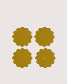 Four mustard yellow, scalloped-edge Merino wool coasters by Graf Lantz, inspired by Japanese floral crests, are arranged in a grid on a white background. One coaster features subtle graf lantz text, adding stylish surface protection.