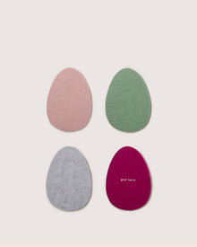 Four Merino wool, egg-shaped coasters by Graf Lantz come in pastel pink, green, gray, and maroon. The maroon coaster features Graf Lantz in white on its surface.