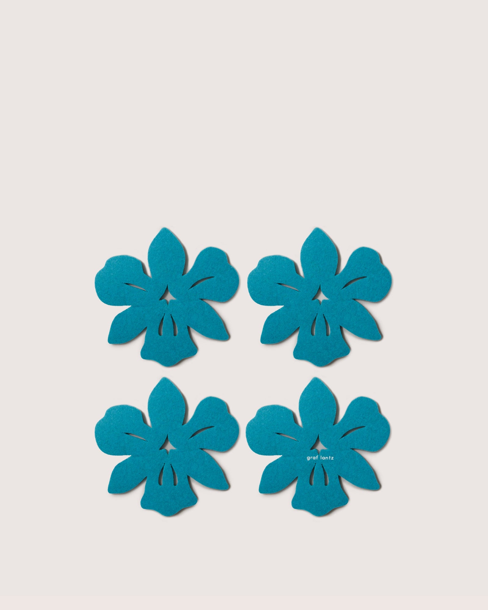 Four blue, flat flower cutouts by Graf Lantz—crafted from premium German Merino wool—are arranged in a grid on a plain white background, making these coasters both sustainable and biodegradable.