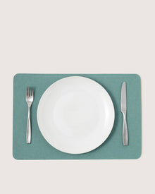 A white empty plate sits centered on a green Graf Lantz Merino wool placemat, with a silver fork to the left and knife to the right, creating stylish designer table decor against a light background.