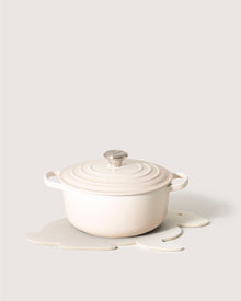 A round, ceramic cream-colored pot with handles and a matching lid from Graf Lantz rests on their exclusive Merino Wool Bunny Trivet. This minimalist setup elegantly sits on a white surface against a neutral background, showcasing its unique blend of style and function.