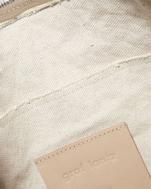 Close-up of beige canvas with a stitched seam and tan Vachetta leather patch embossed with Graf Lantz, sewn onto the fabric. It hints at the timeless elegance of a Hana Hobo bag. The top edge shows part of a zipper.