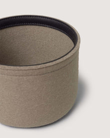 A close-up of a round, beige Merino wool bin by Graf Lantz with a dark inner lining appears against a simple light background. Only part of this sustainable organizer is shown in the frame.