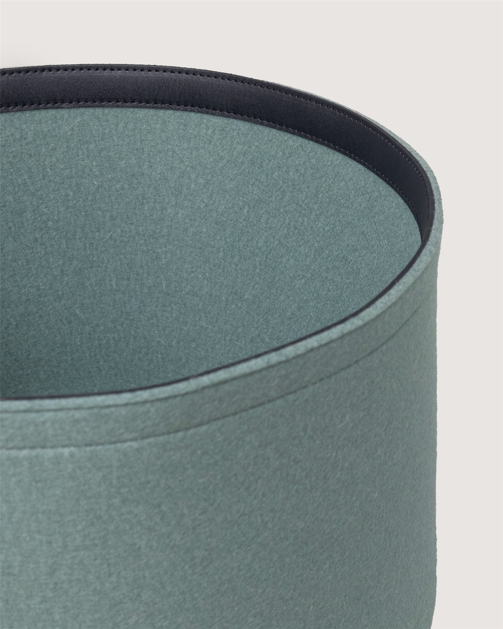 Close-up of the top edge of a round, light blue-green Graf Lantz fabric lampshade with a dark interior lining, set against a plain background—an elegant accent piece for sustainable organization in any room.
