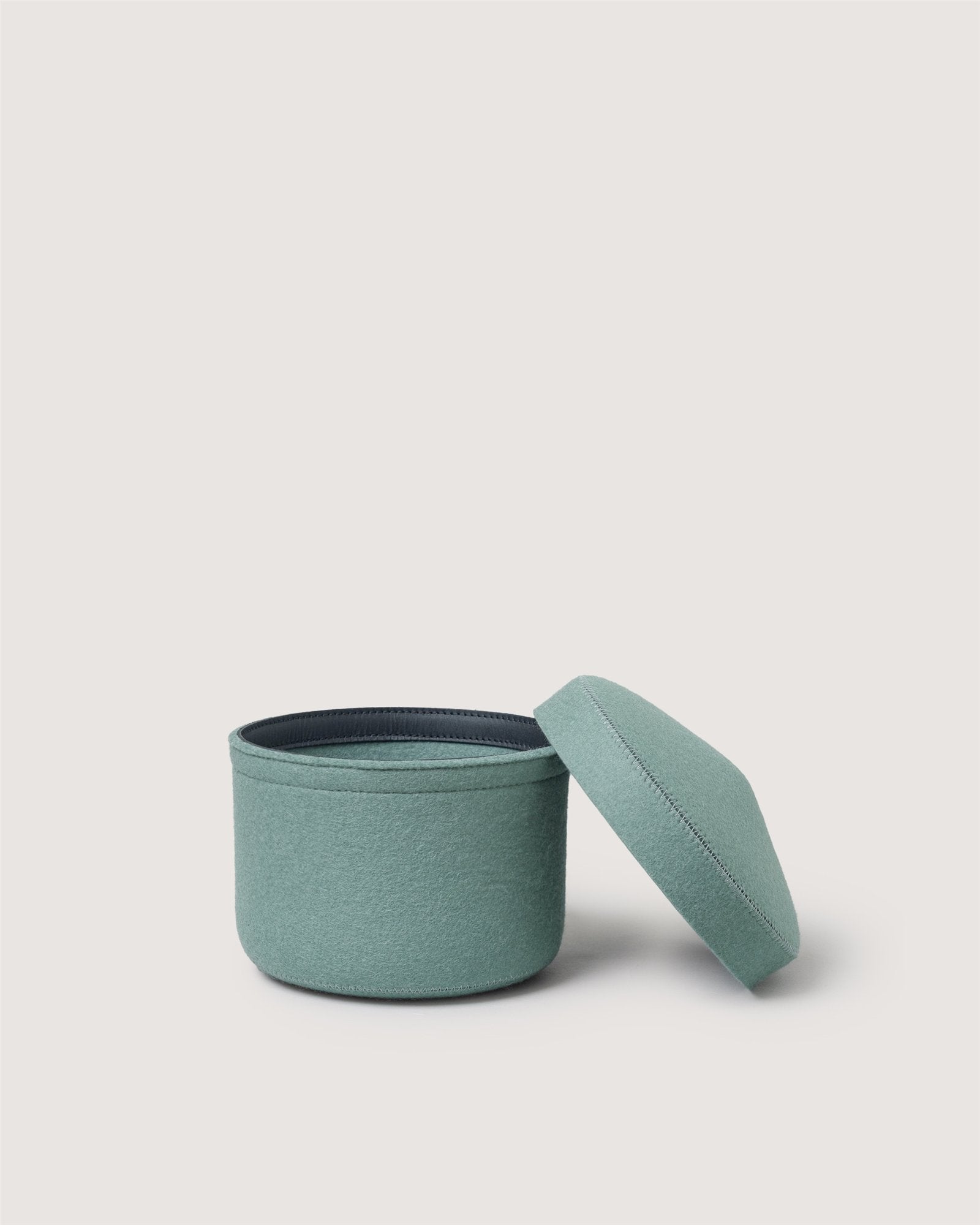A small, round, light teal Merino wool bin by Graf Lantz is shown with its matching removable lid beside it against a plain white background.