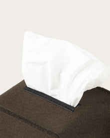 A close-up of a Graf Lantz dark brown tissue box with a white tissue partially pulled out against a plain, light background.